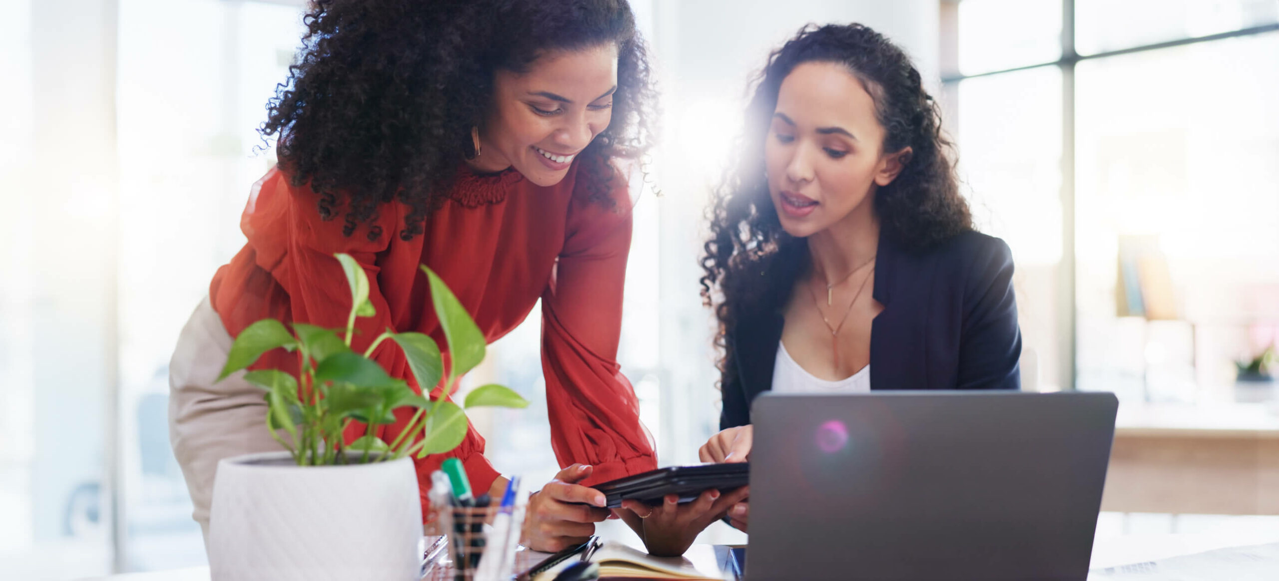 Women-Talking-at-Desk-Laptop-Green-Plant-iStock-1962581684-scaled.jpg