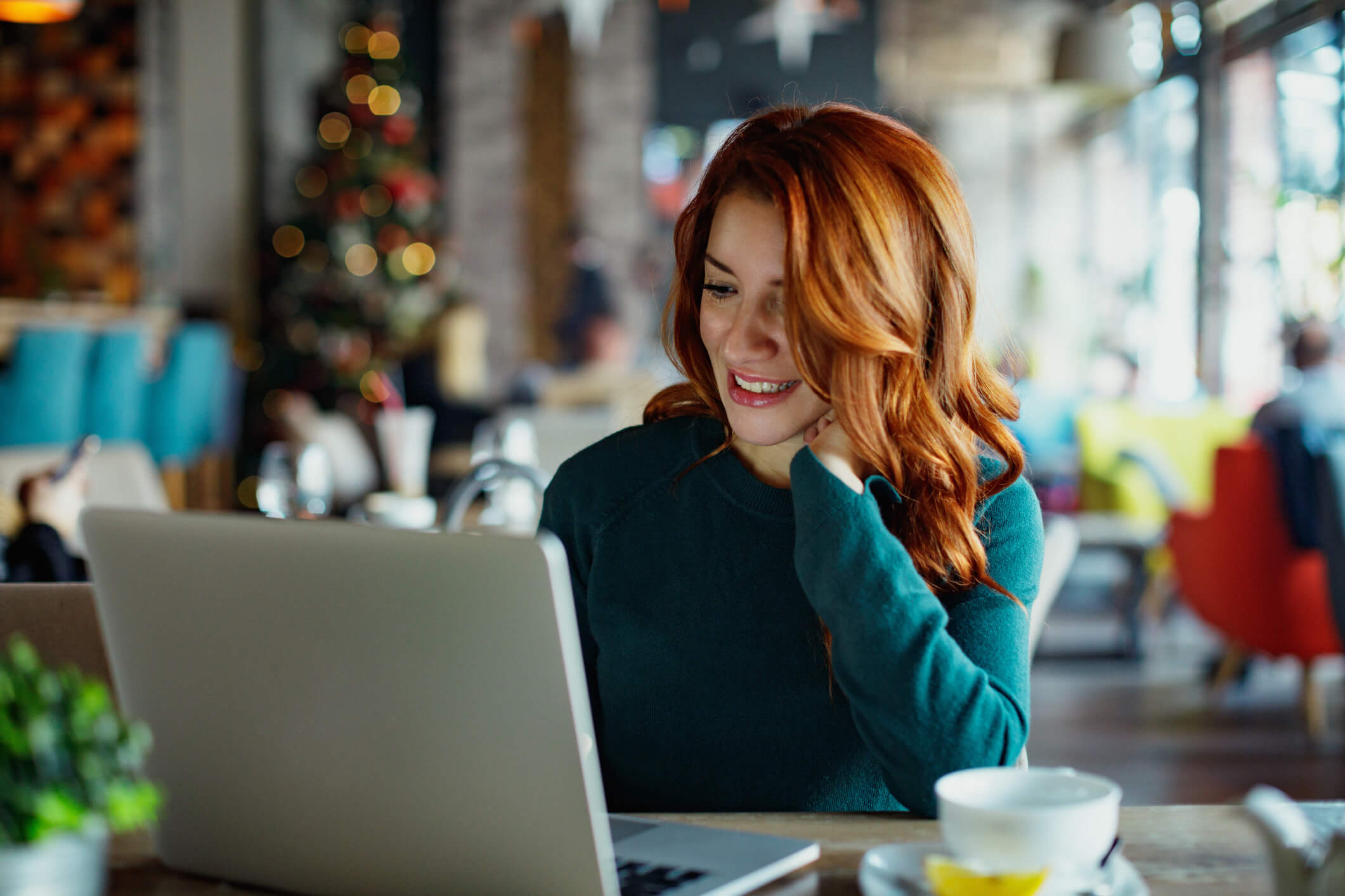 Woman-Green-Sweater-Looking-at-Laptop-Christmas-Trees-Background-iStock-1078020954.jpg